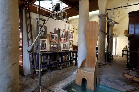 Ambiente laterale del chiostro con sedia della serie "Mobili nella valle" di Mario Ceroli, legno Pino grezzo, Poltronova, 1972 (in primo piano); installazione fotografica di Maurizio Marzadori con scale a pioli e bancone industriale di recupero (sullo sfondo a sinistra). Foto © Paolo Righi, Bologna.